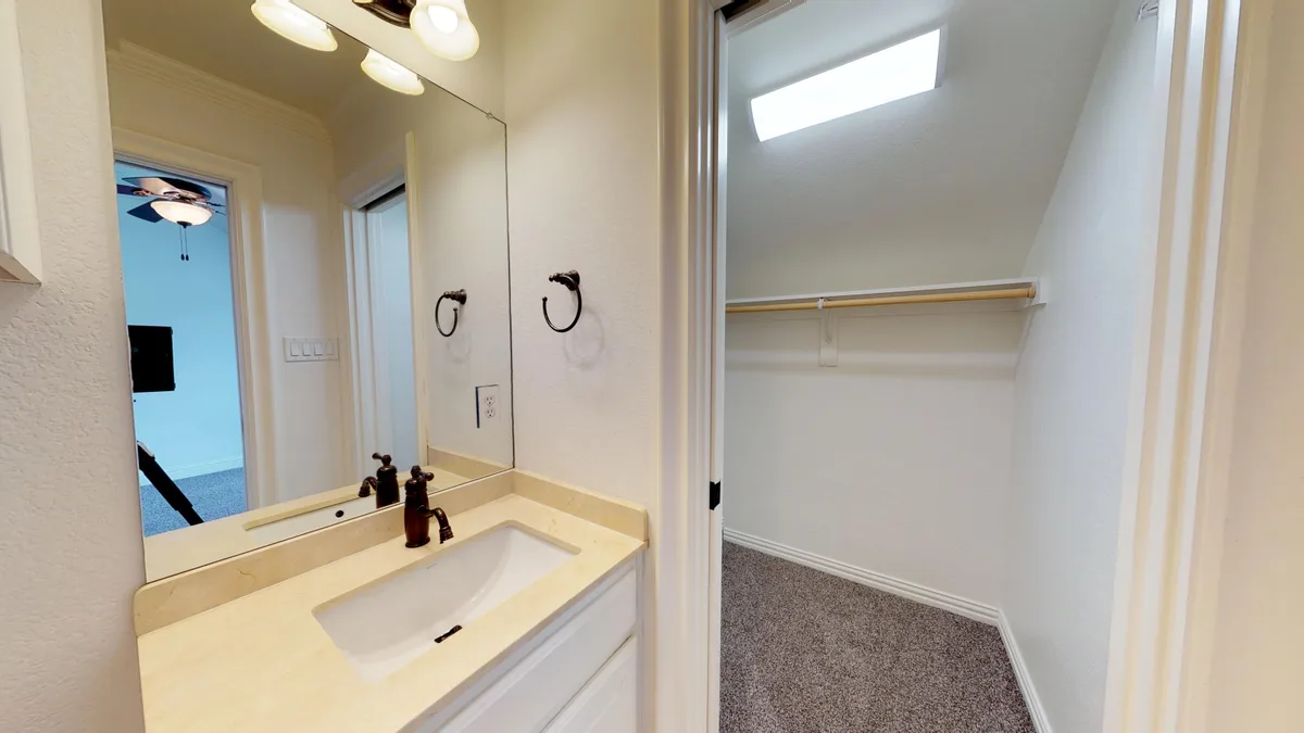 Vanity with marble top and large mirror opening onto a walk-in closet lit by a skylight