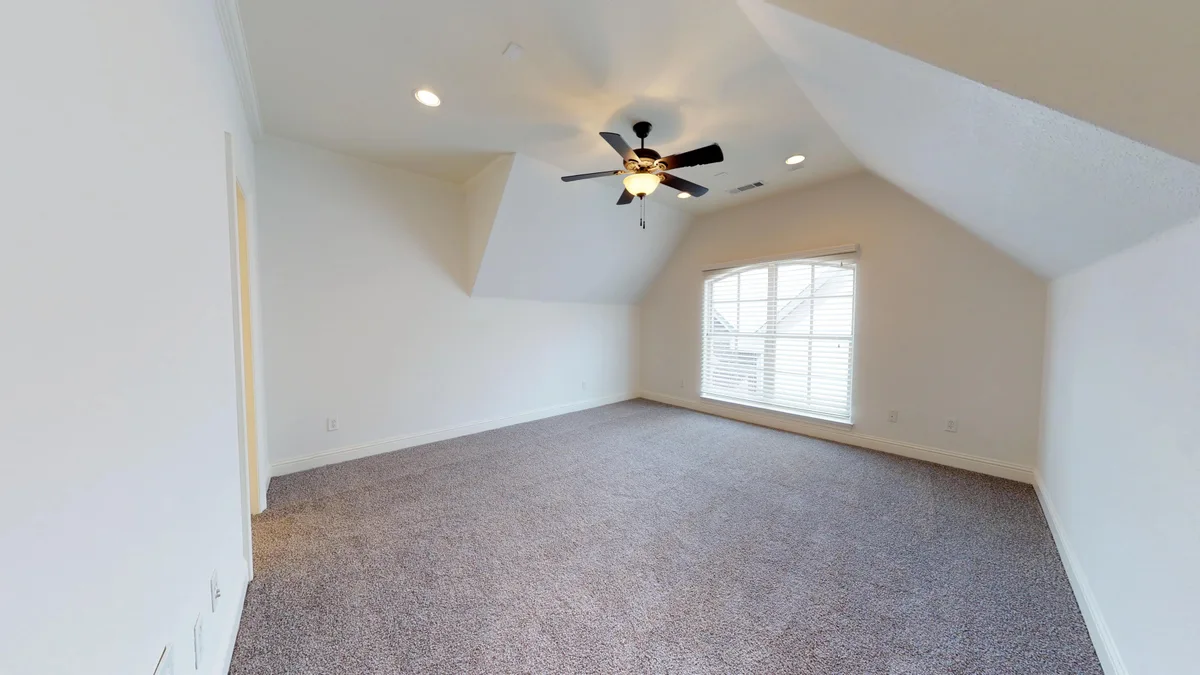 Carpeted bedroom with a vaulted ceiling, dark ceiling fan, and a tall window