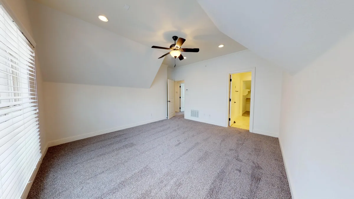 Carpeted bedroom with sloped ceiling and ceiling fan, opening to an ensuite bathroom