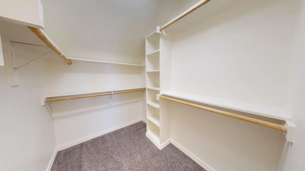 Carpeted walk-in closet with a built-in shelving tower and wood hanging rods