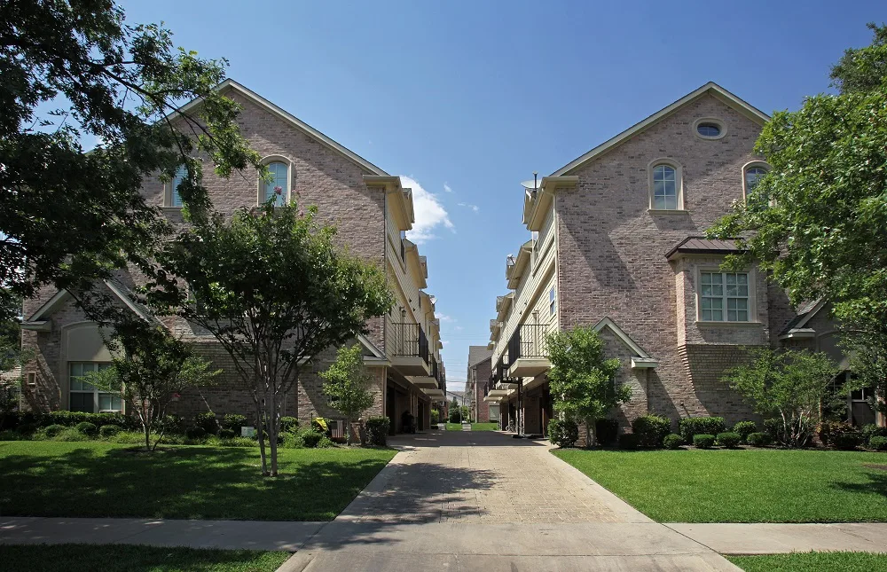 Landscaped walkway and lawns running between two brick townhome buildings under a clear sky