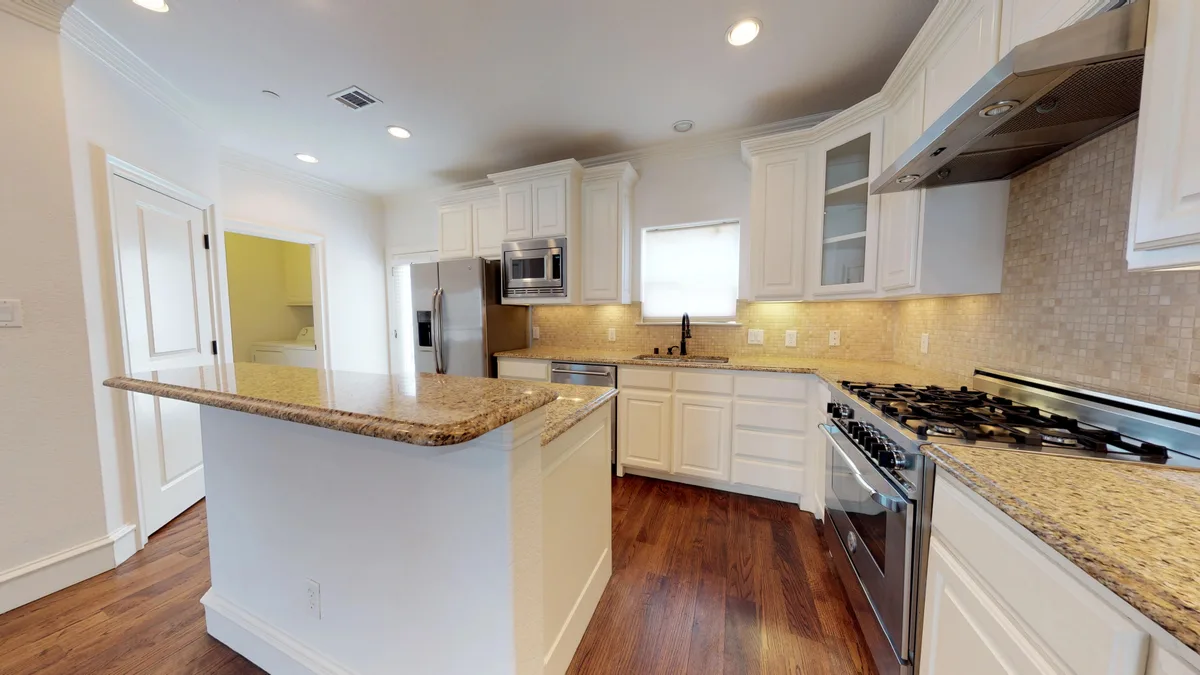 Kitchen with granite island, white cabinets, stainless gas range, and mosaic tile backsplash