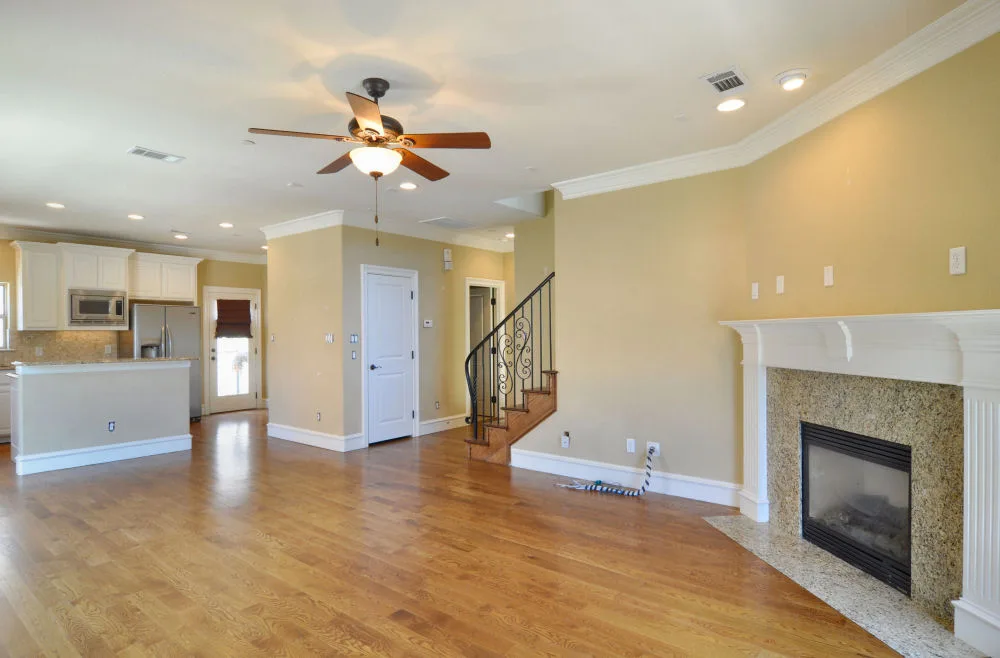 Open living room with hardwood floors, corner granite-surround fireplace, ceiling fan, and staircase