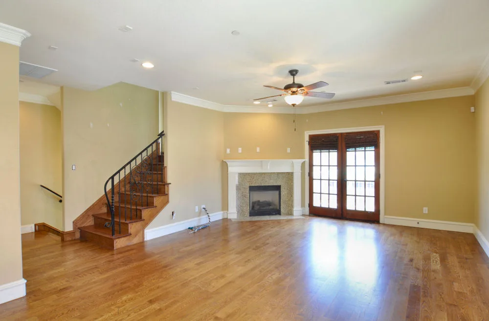 Living room with hardwood floors, marble-front fireplace, iron-rail staircase, and French doors