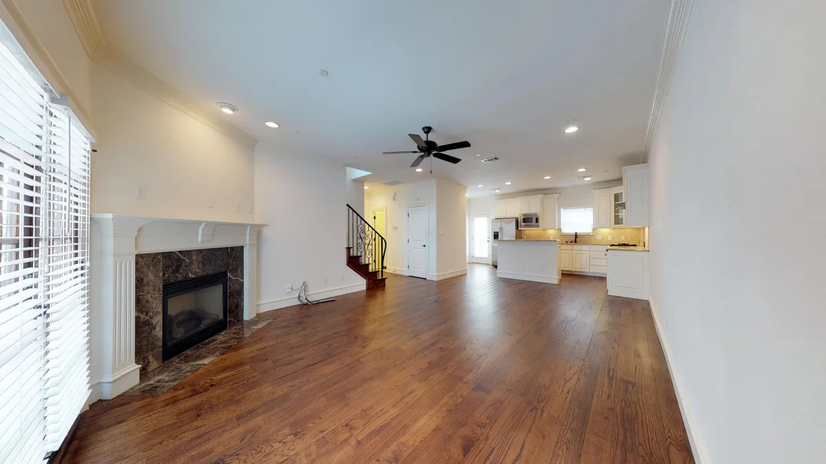 Wide great room opening to the kitchen, with hardwood floors, marble fireplace, and staircase