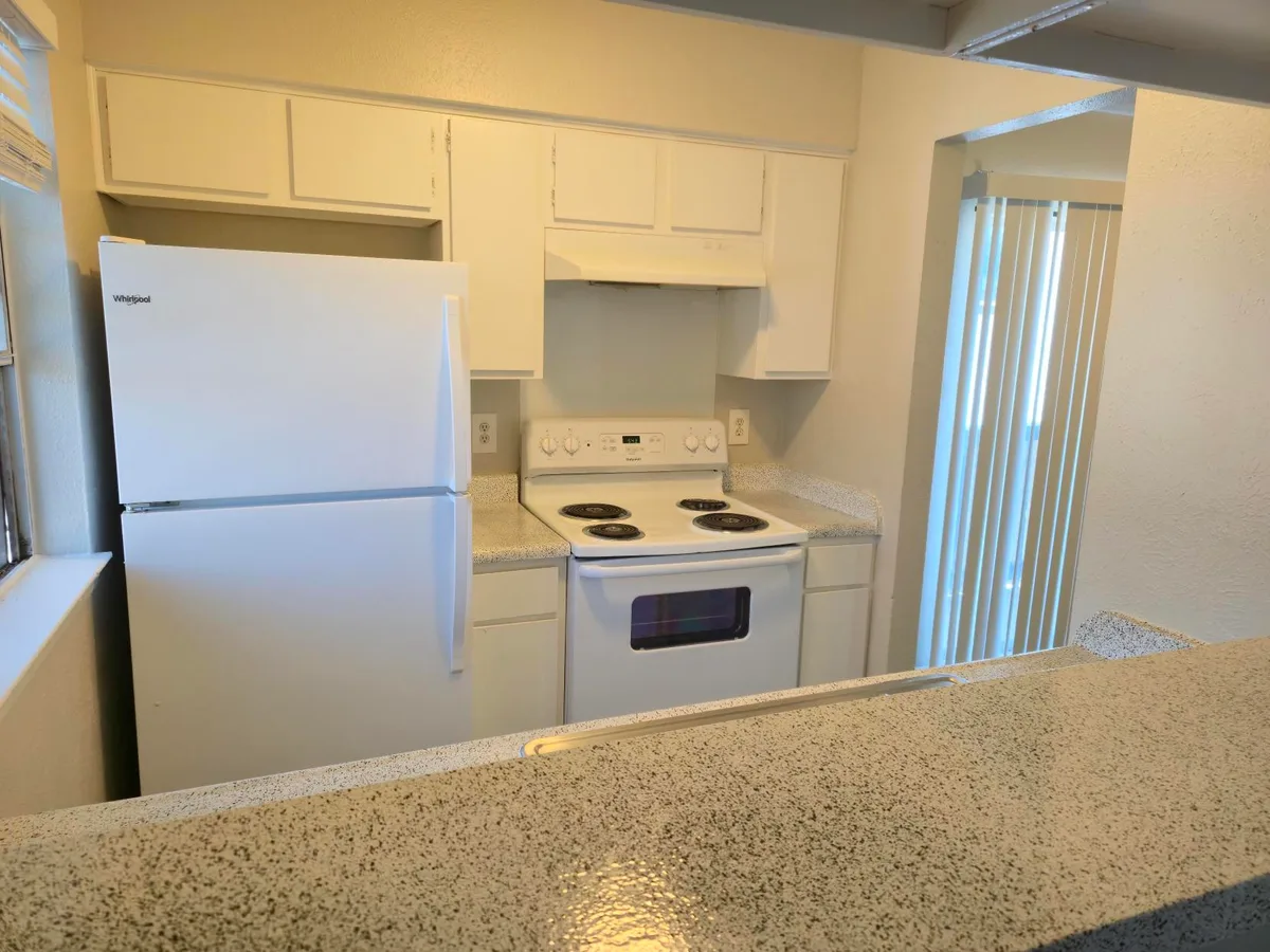 Galley kitchen with white cabinetry, white appliances, and a breakfast-bar pass-through to the living area
