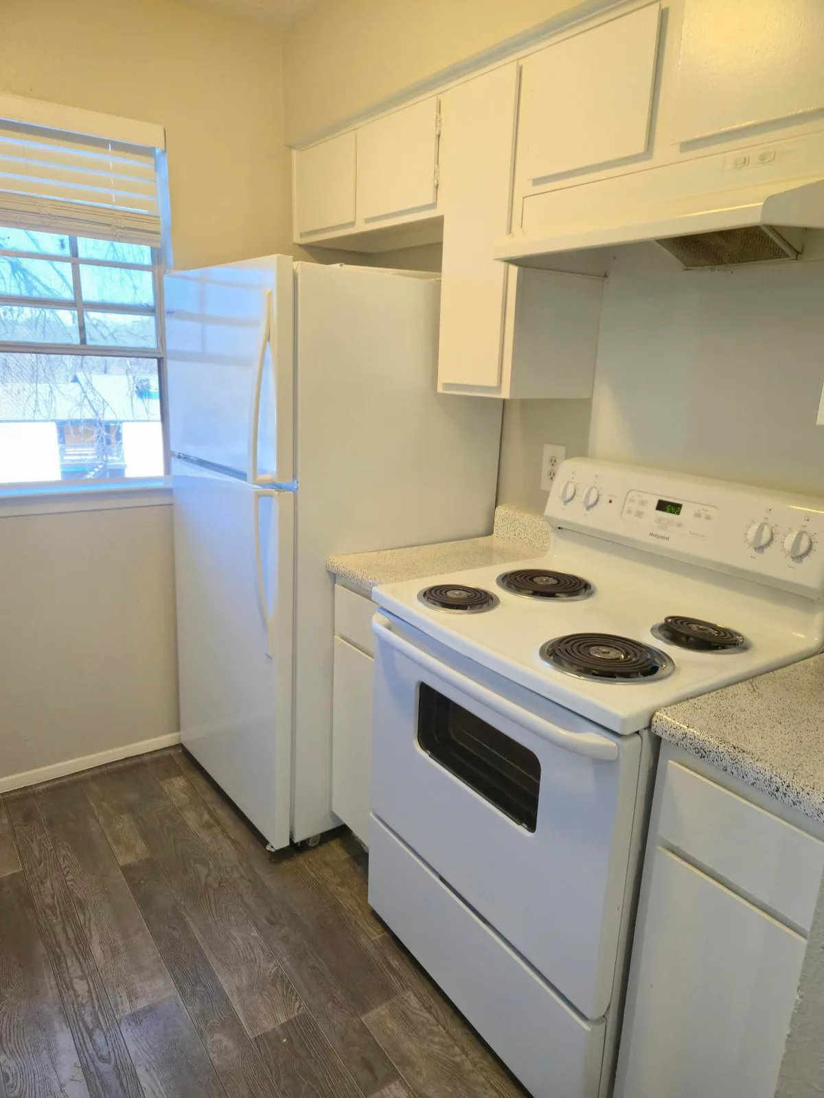 Kitchen with a white electric range and refrigerator beside a window, over wood-style plank flooring