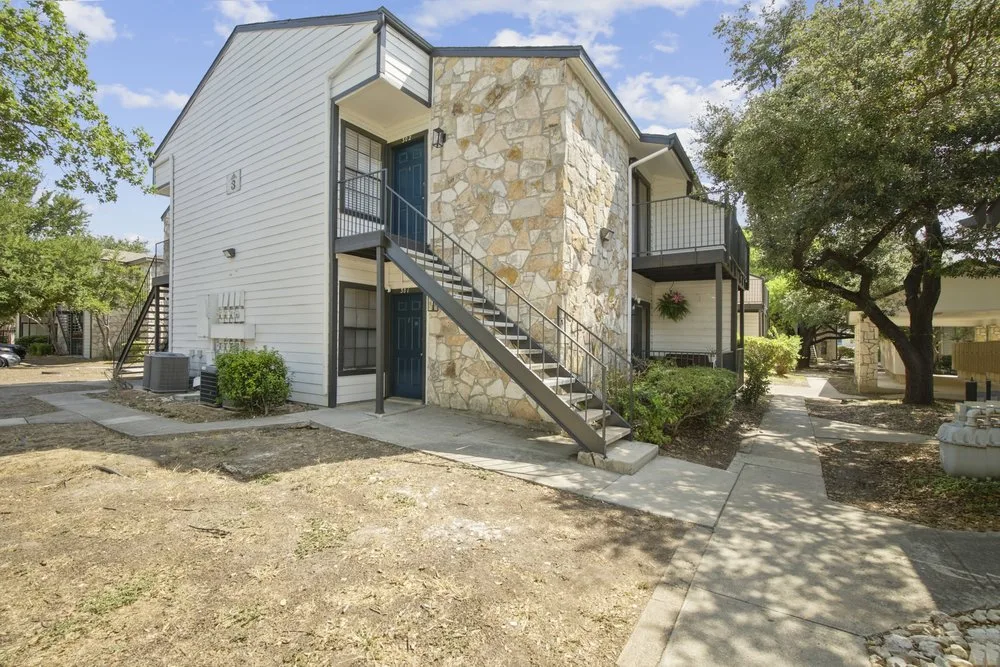 Corner view of a stone-and-siding apartment building with a metal exterior staircase and landscaped walkways