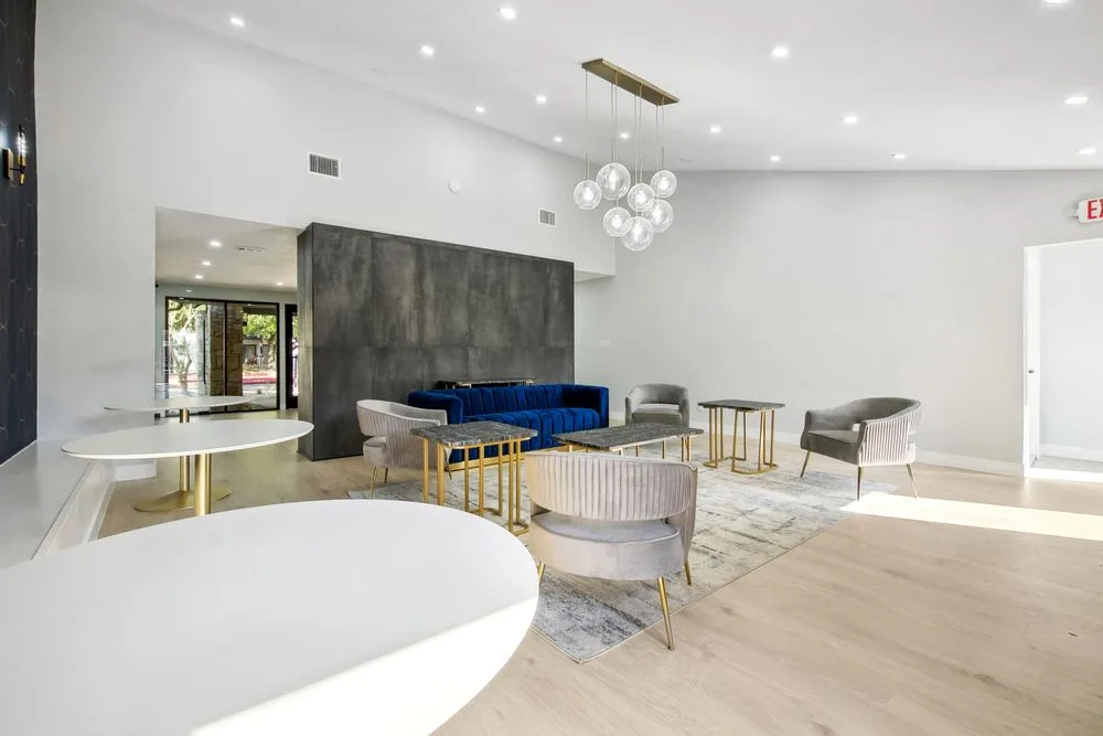 Renovated resident lounge with a blue velvet sofa, gray accent chairs, gold-legged tables, and a globe chandelier