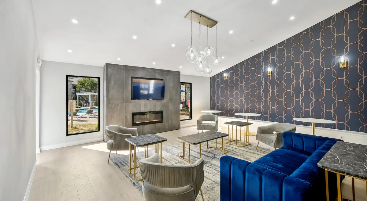 Renovated resident lounge with a linear fireplace below a mounted TV, navy patterned wall, and blue velvet seating