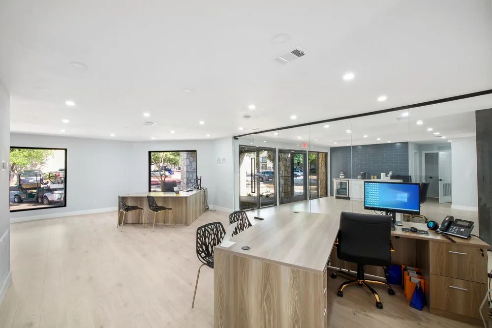 Bright leasing office with wood reception desks, a glass-walled conference room, and modern seating