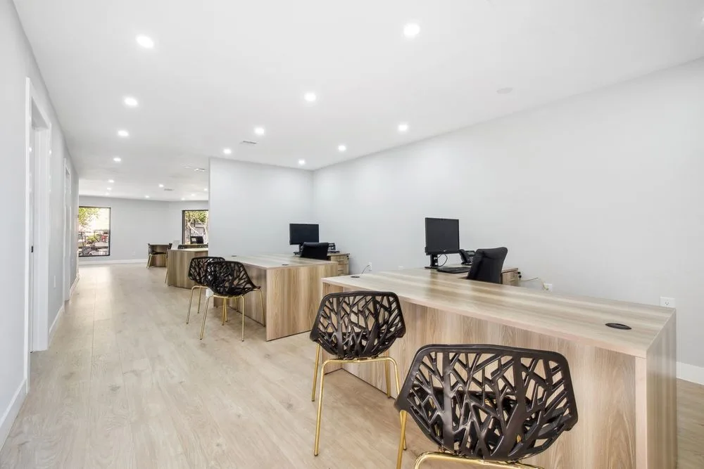 Leasing office workstations in light wood with black lattice-back chairs under recessed lighting