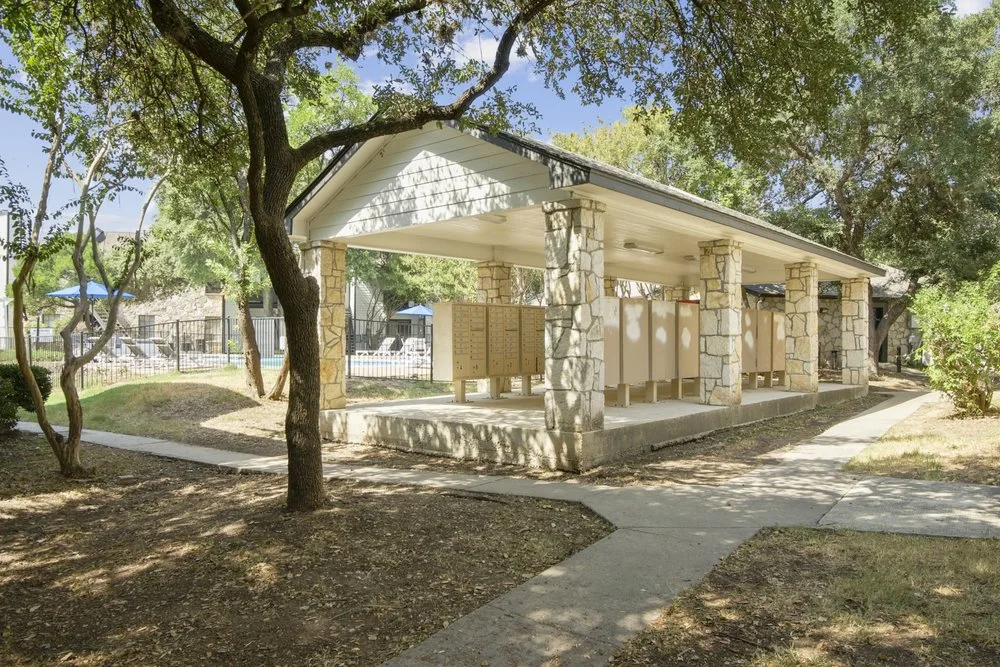 Covered stone picnic pavilion with cluster mailboxes beside shaded walking paths and the pool
