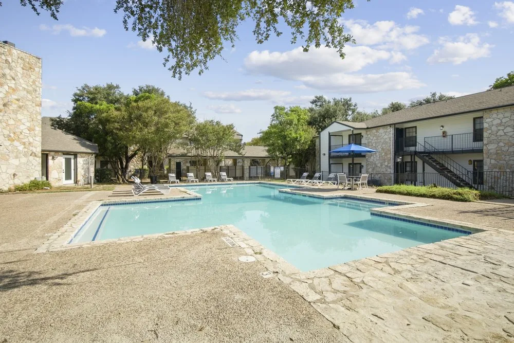 Resort-style pool and sundeck bordered by stone apartment buildings and mature trees
