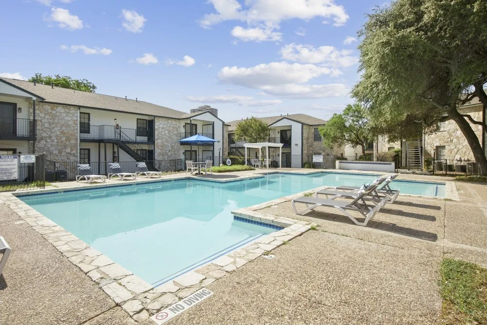 Swimming pool with lounge chairs and a pergola set against two-story stone residences