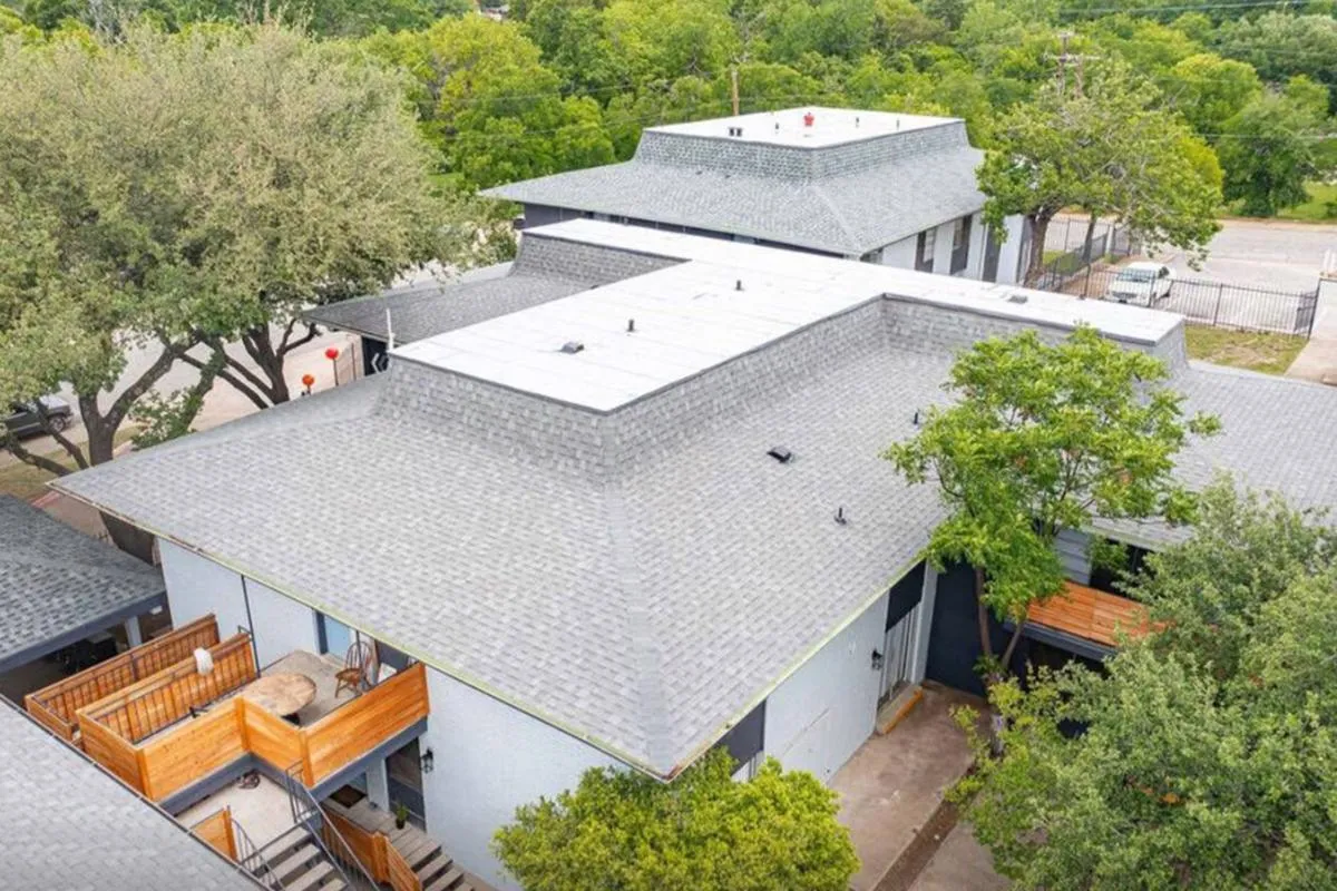 Aerial view of gray shingle rooftops, wood balcony rails, and surrounding trees at La Madera in Dallas
