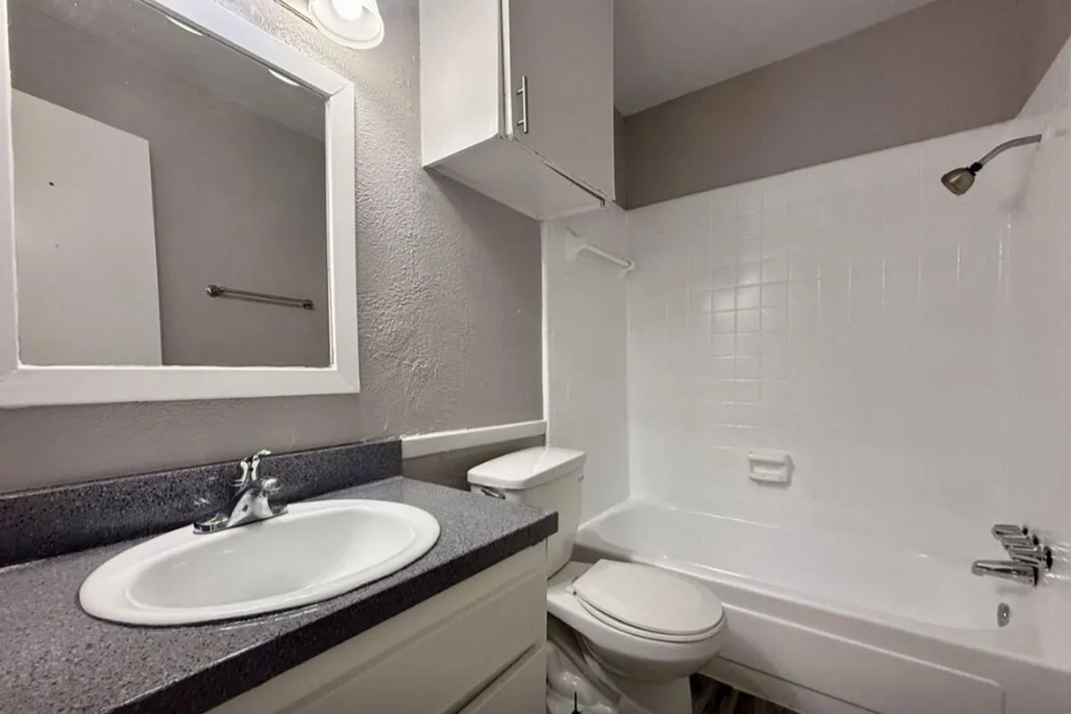 Bathroom with gray countertop vanity, framed mirror, and white tiled tub surround at La Madera in Dallas