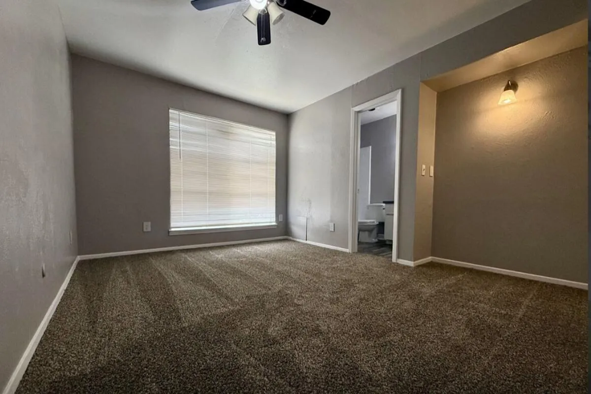 Carpeted bedroom with ceiling fan, window with blinds, and attached bathroom at La Madera in Dallas