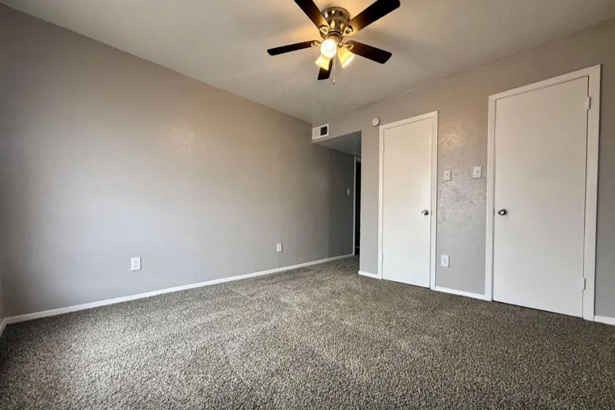 Carpeted bedroom with ceiling fan and two white closet doors at La Madera in Dallas