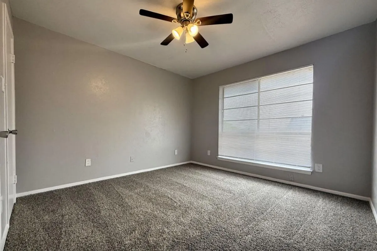 Carpeted bedroom with ceiling fan and window with mini blinds at La Madera in Dallas