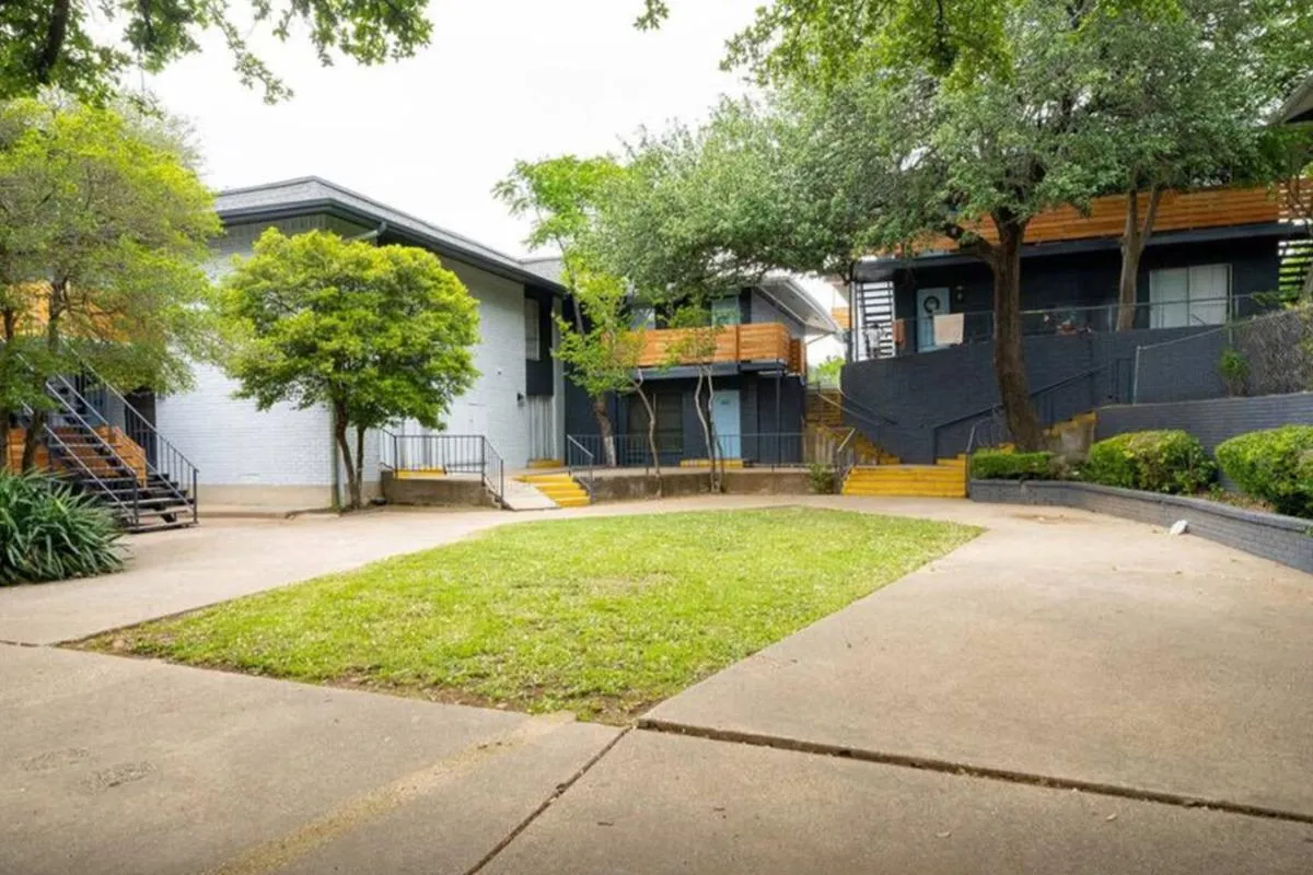 Courtyard lawn with sidewalks between white and dark-navy two-story buildings at La Madera in Dallas
