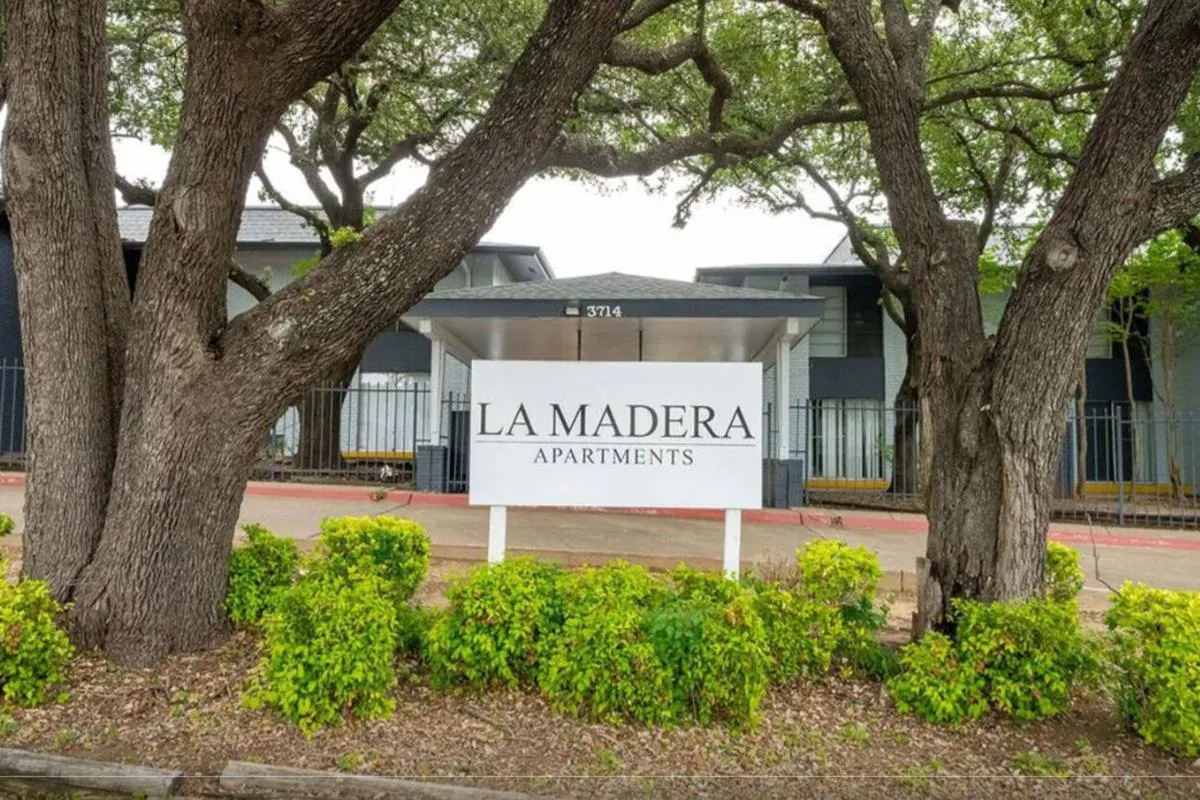 Entrance drive with La Madera Apartments sign, oak trees, and covered entry canopy at La Madera in Dallas