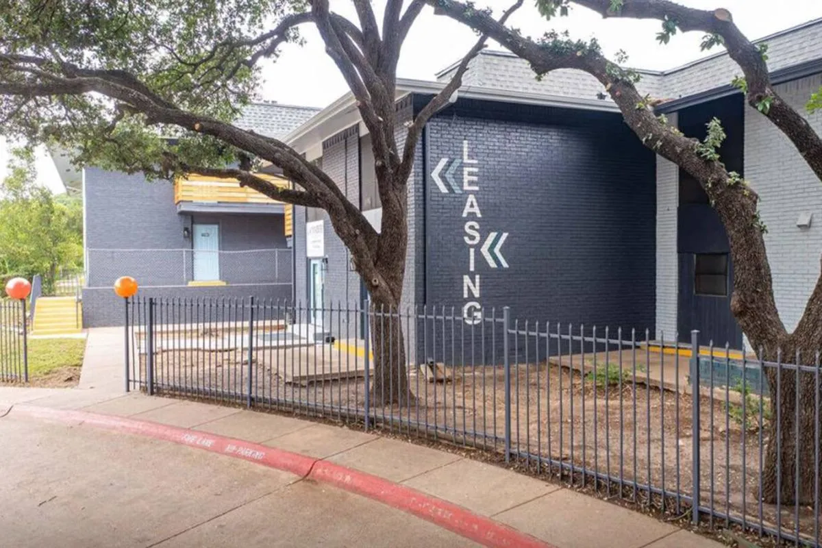 Dark-navy brick wall painted with a leasing sign and arrows behind an iron fence at La Madera in Dallas