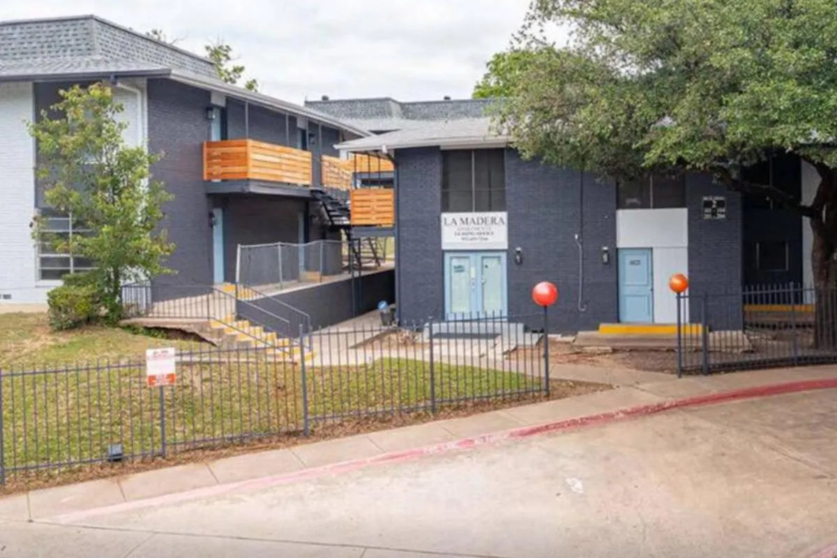 Dark-navy brick leasing office entrance with light-blue doors and iron fence at La Madera in Dallas