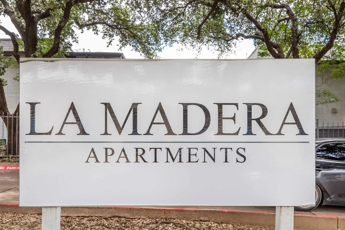 White La Madera Apartments monument sign beneath oak trees at La Madera in Dallas