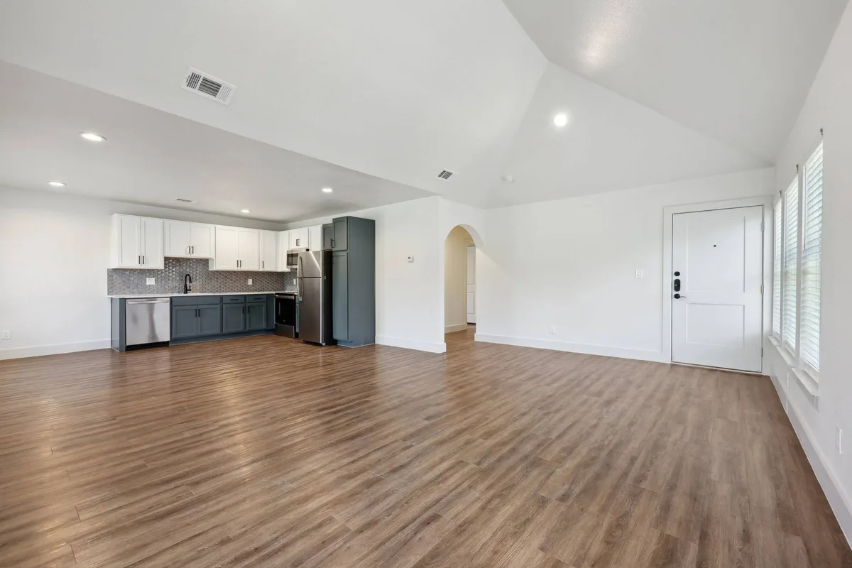 Open-concept living space with a vaulted ceiling, an arched hallway, and a kitchen along the far wall
