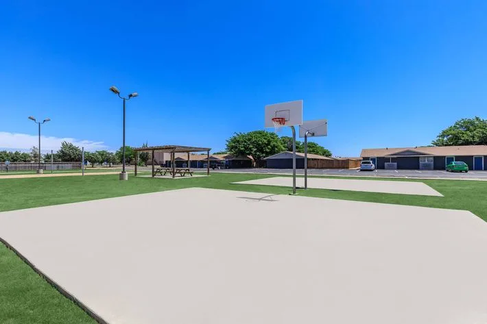 Outdoor basketball court with a hoop and green turf surround, next to a pergola and picnic area