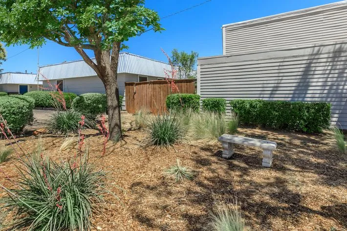 Landscaped community grounds with a concrete bench, red yucca, and ornamental grasses between the buildings