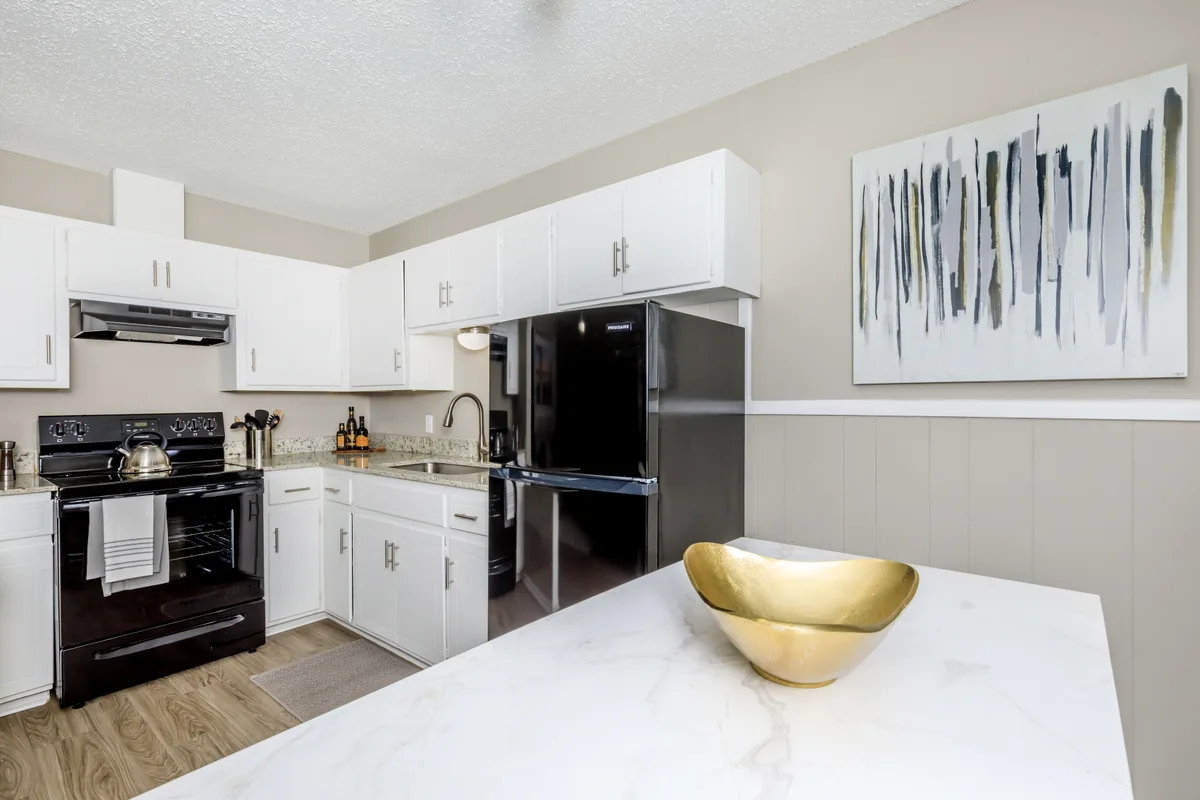 Kitchen with white cabinetry, a black refrigerator and range, granite-style counters, and a waterfall breakfast bar