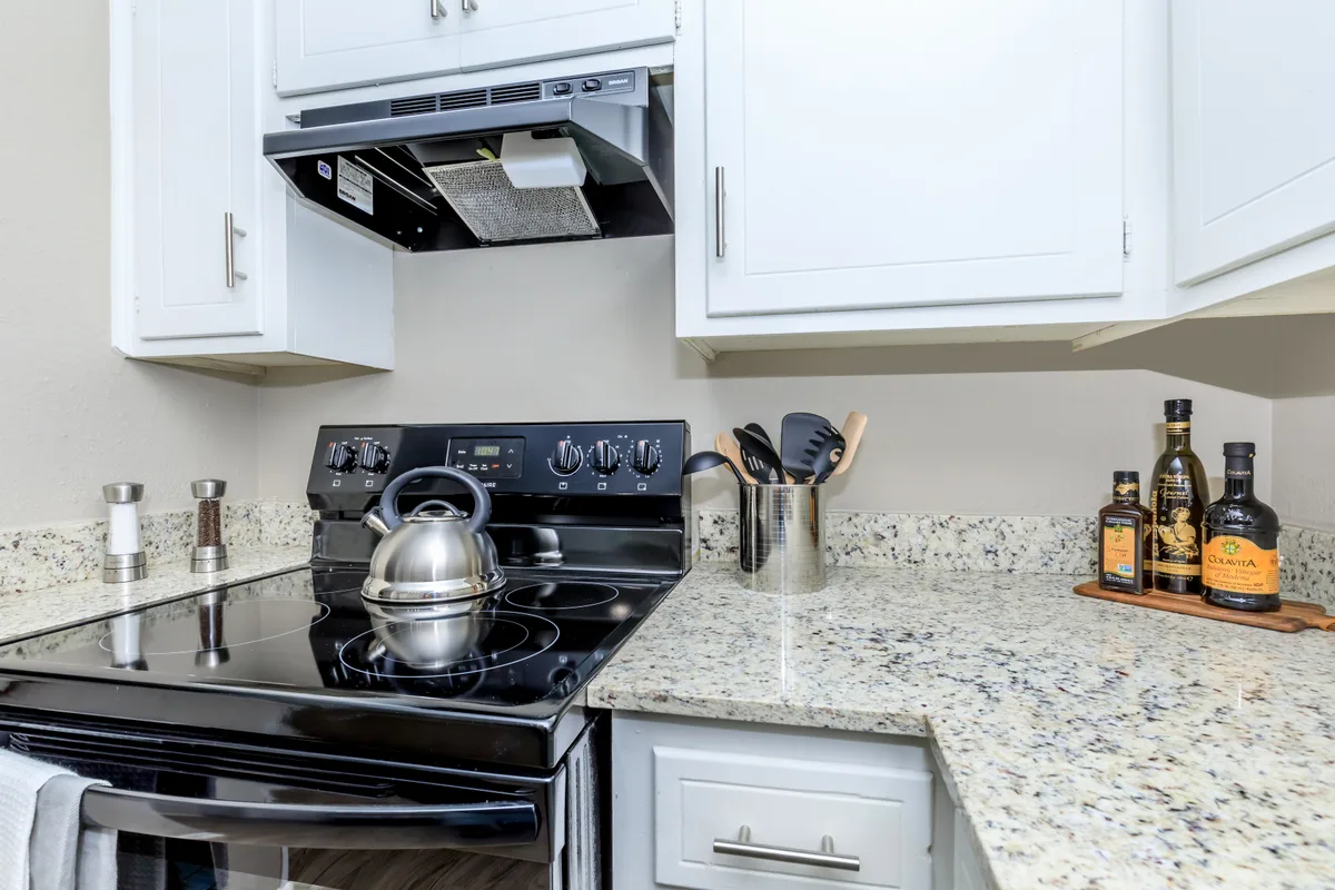 Kitchen detail of a black glass-top electric range beneath white cabinets and a speckled granite-style counter