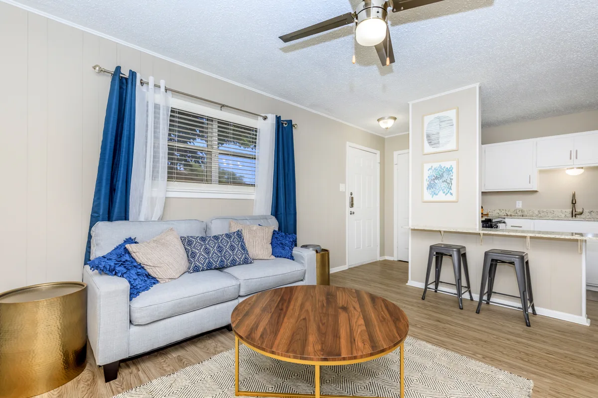 Living room with wood-look flooring, a ceiling fan, and a breakfast bar with metal stools opening to the kitchen