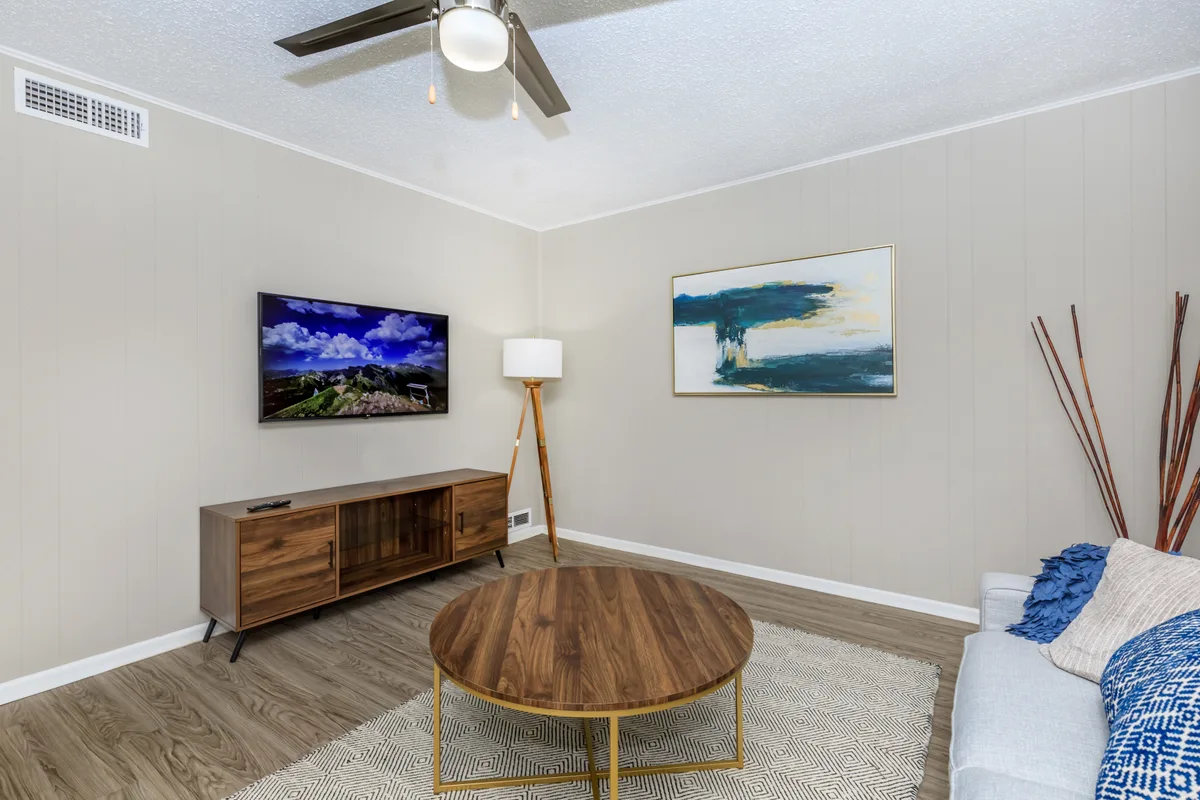 Open living area with greige walls, wood-look plank floors, a media console, and mounted television
