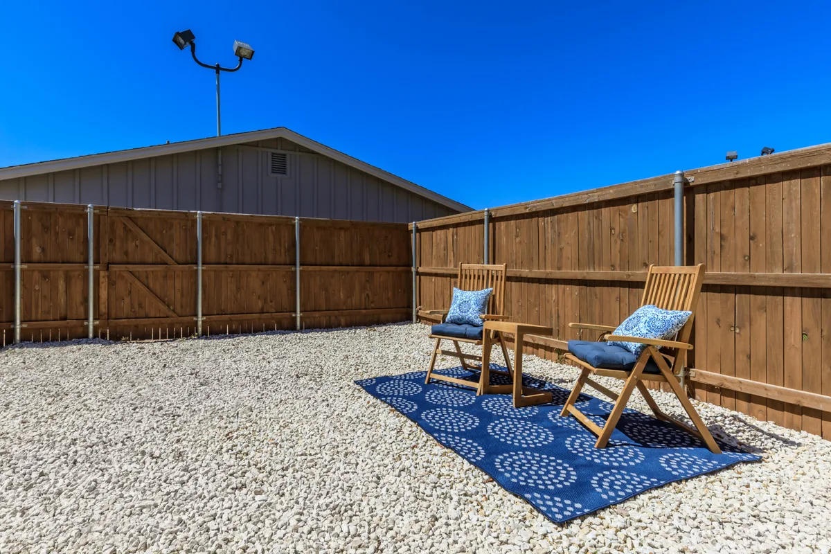 Private fenced patio with white river-rock gravel, a blue outdoor rug, and wood folding chairs with blue cushions