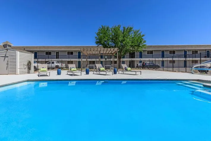 Sparkling blue swimming pool with poolside lounge chairs and a two-story residential building behind
