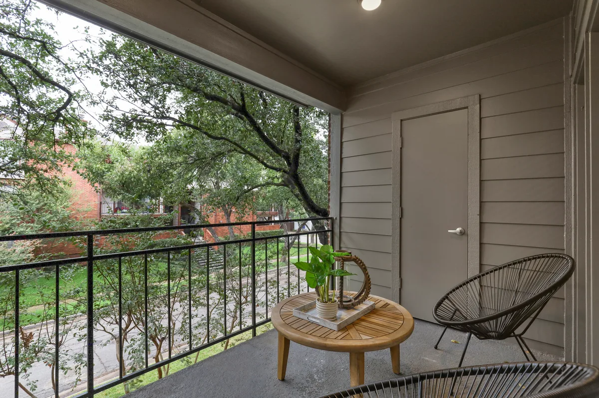 Private covered balcony with lounge chair, wood side table, and leafy tree views