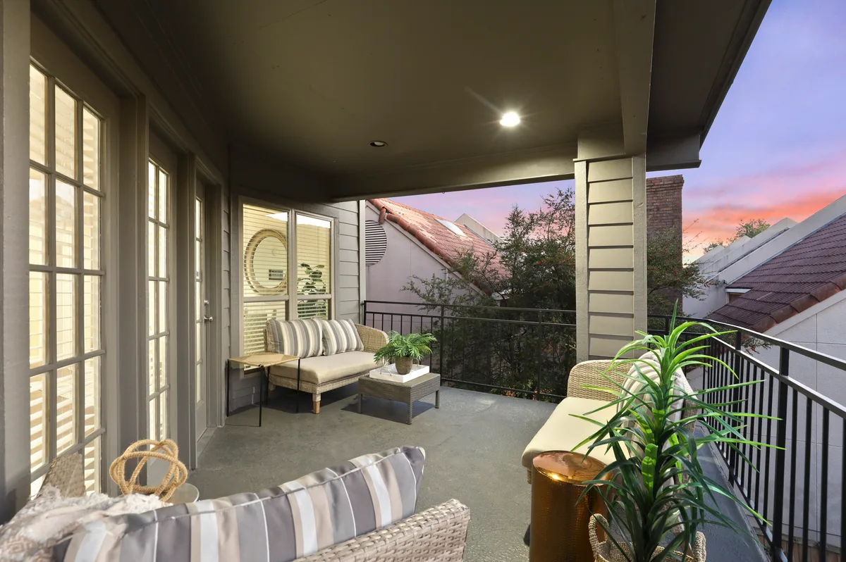 Private covered balcony staged with wicker seating and rooftop views at dusk