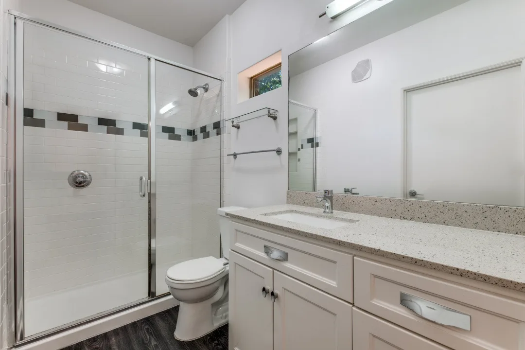 Bathroom with walk-in glass shower, quartz vanity, and mosaic tile accent band