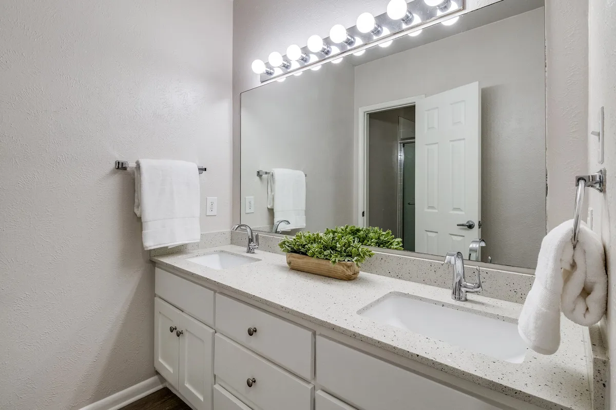 Bathroom with dual-sink quartz vanity and large framed mirror under bulb lighting