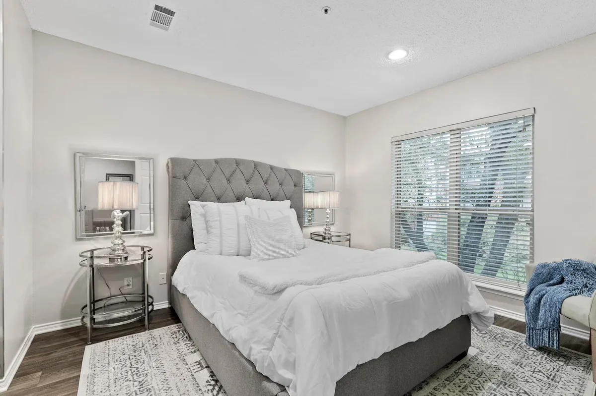 Staged bedroom with tufted gray headboard, large window, and wood-look flooring