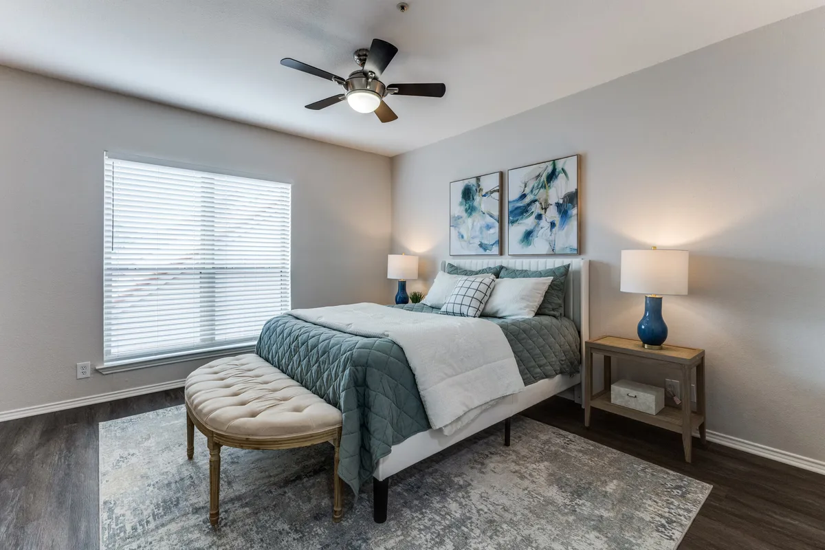 Staged bedroom with ceiling fan, teal bedding, and wood-look flooring