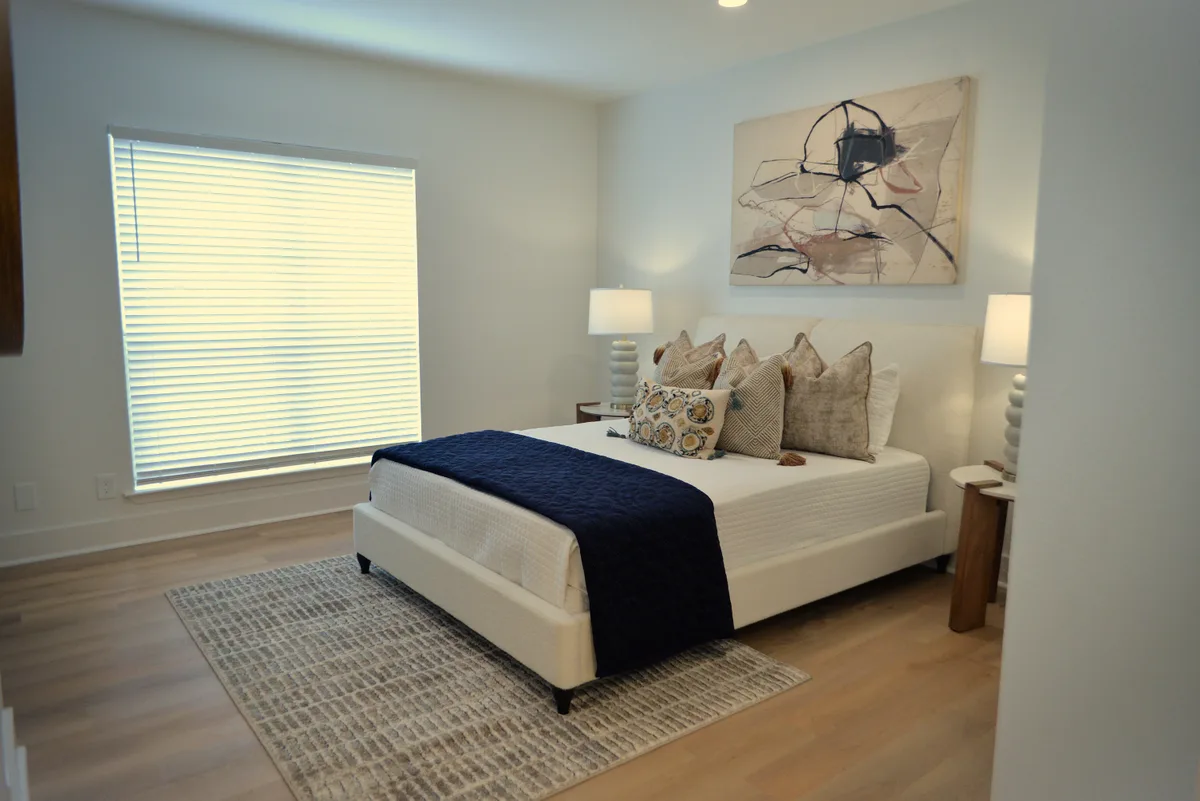 Staged bedroom with upholstered bed, navy accents, and wood-look flooring