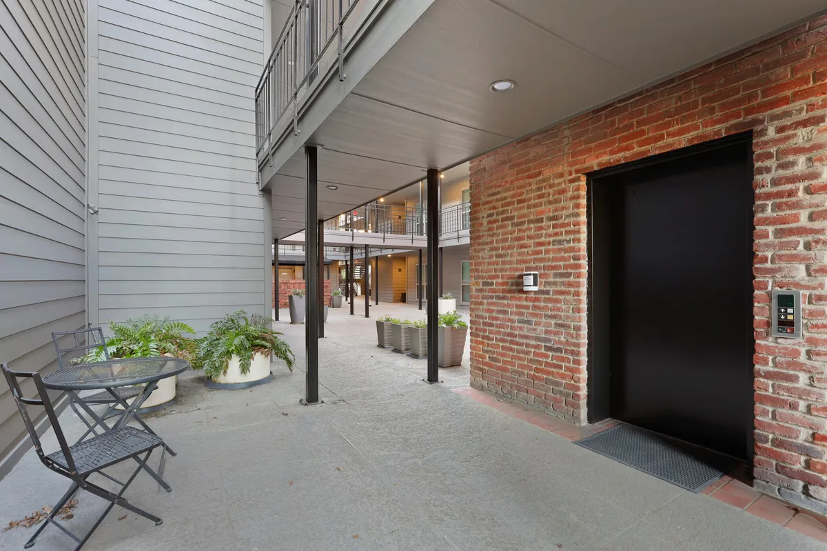 Ground-floor breezeway with bistro seating, potted plants, and elevator access