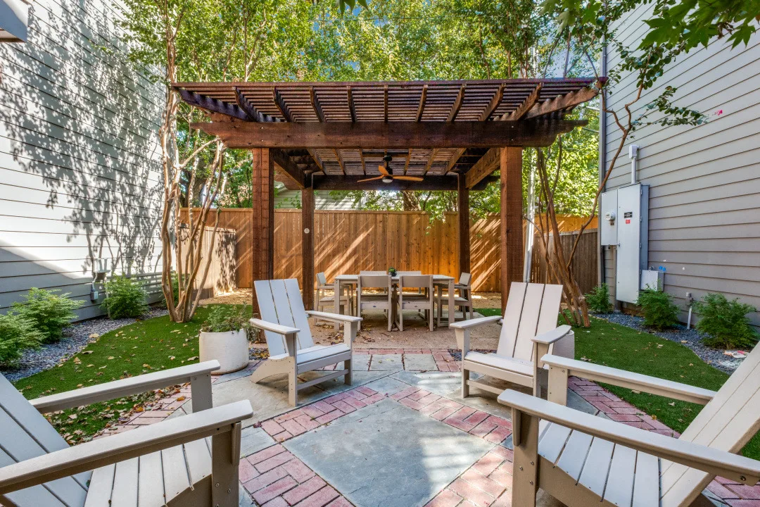 Pergola-shaded dining area with Adirondack chairs on a turf-lined brick patio