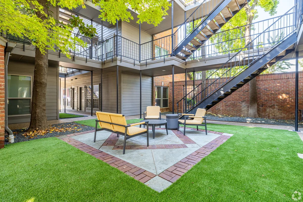 Interior courtyard with woven lounge chairs beneath an exterior staircase and brick wall
