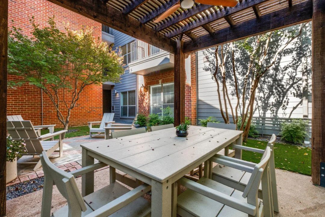 Covered pergola dining table framed by crepe myrtles in a brick courtyard