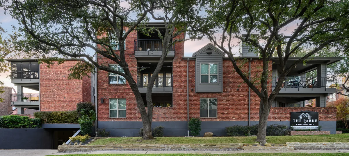 Brick building exterior with mature oak trees and The Parke at University Park monument sign